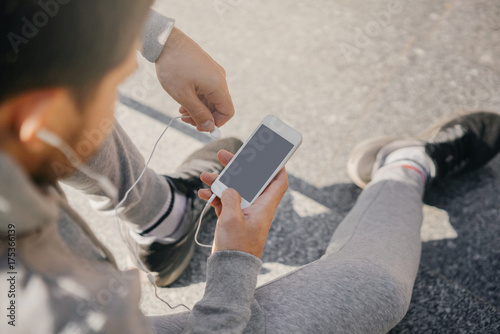 man athlete sitting on the street with mobile phone, listening to music. City workout with smart gadgets and sport applications. photo