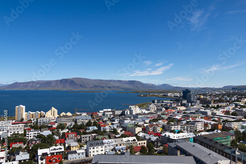 Aerial view on capital of Iceland - city of Reykjavik - ocean bay, hills, mountains, green medows, roadways, vehicles, streets, houses, traffic, roofing - on sunny day. © Studio Dagdagaz