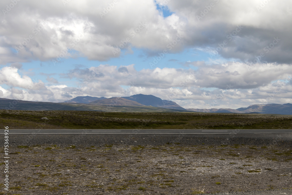 Iceland landscape with fields, mountains, sky, clouds, road and hills. Copy space.