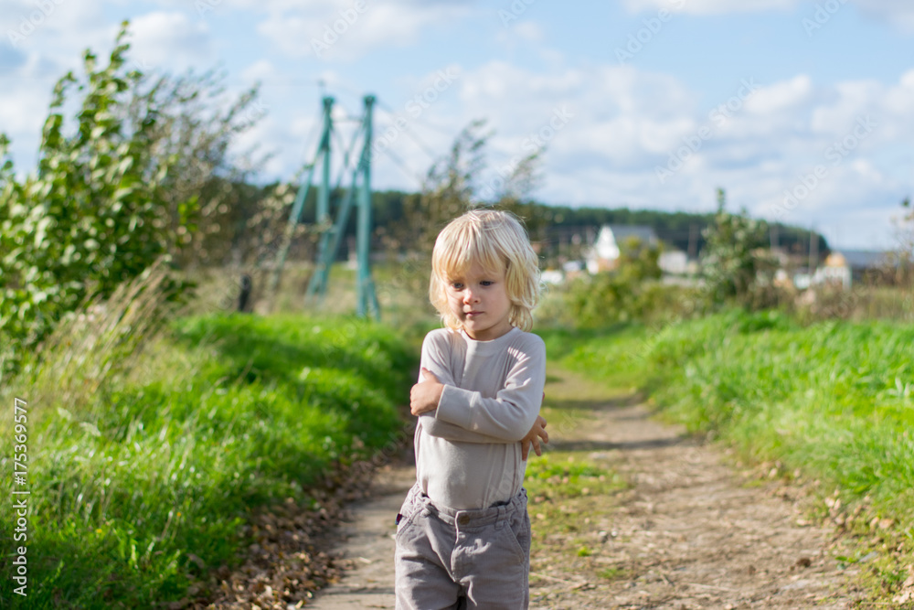 Seriouse blond boy staying embraced himself with his arms, country road to the Urals village
