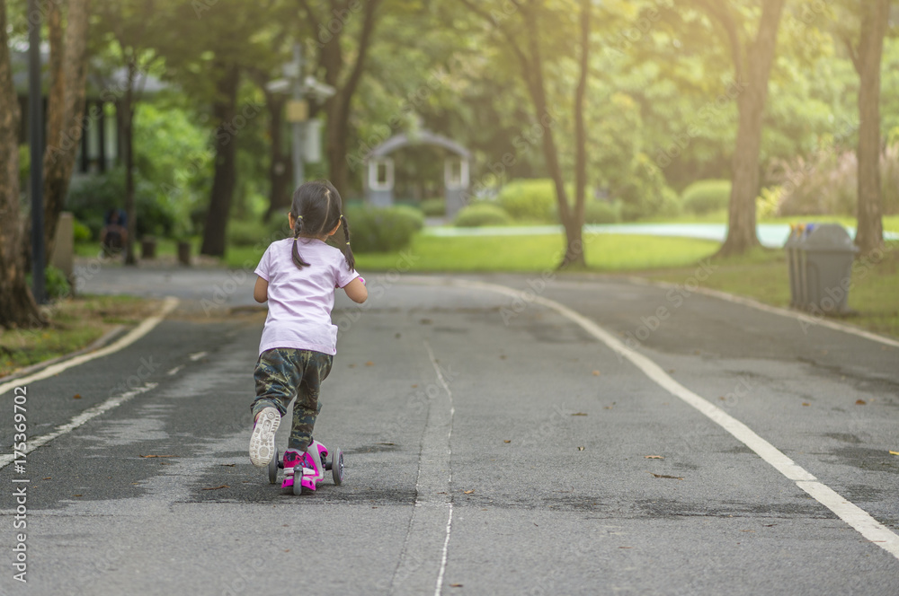 Child riding scooter in park or Behind child riding scooter