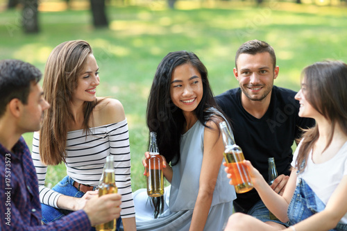Cheerful people sitting on blanket, drinking beer and talking outdoors