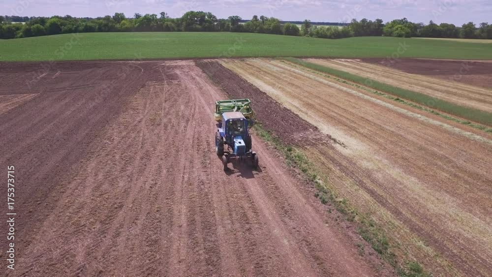 Agricultural tractor with trailer for plowing working on arable field. Aerial view farming tractor driving on plowed field. Farming equipment on field. Agricultural industry. Agriculture machine work Agricultural tractor with trailer for plowing working on arable field. Aerial view farming tractor driving on plowed field. Farming equipment on field. Agricultural industry. Agriculture machine work