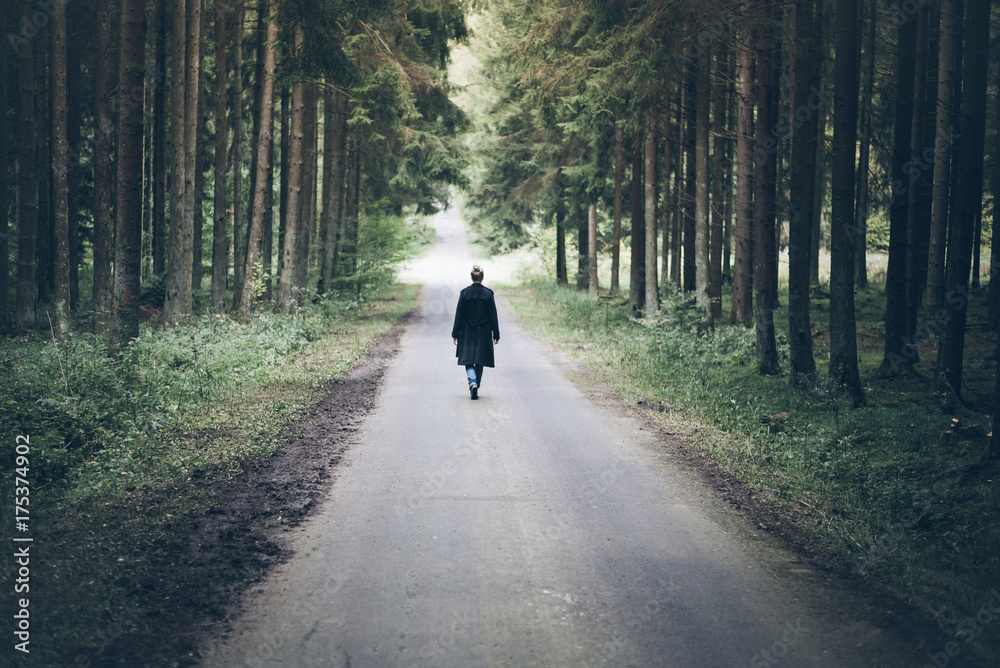 Fototapeta premium young blonde caucasian woman walking on narrow road through dark forest