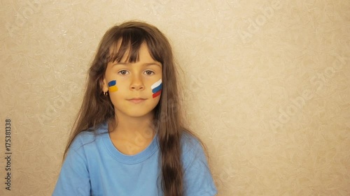 A child with painted flags of Russia and Ukraine. The face of a little girl with the flags of Russia and Ukraine. photo