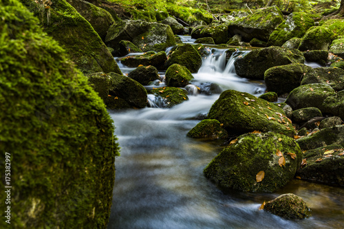 Waterfall falling on stones through autumn forest. Fall nature specification. Stones along and in the river in forest.