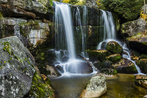 Waterfall falling on stones through autumn forest. Fall nature specification.