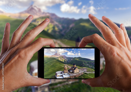 Travel concept. Hands making photo of Gergeti orthodox church high in the mountains, Georgia