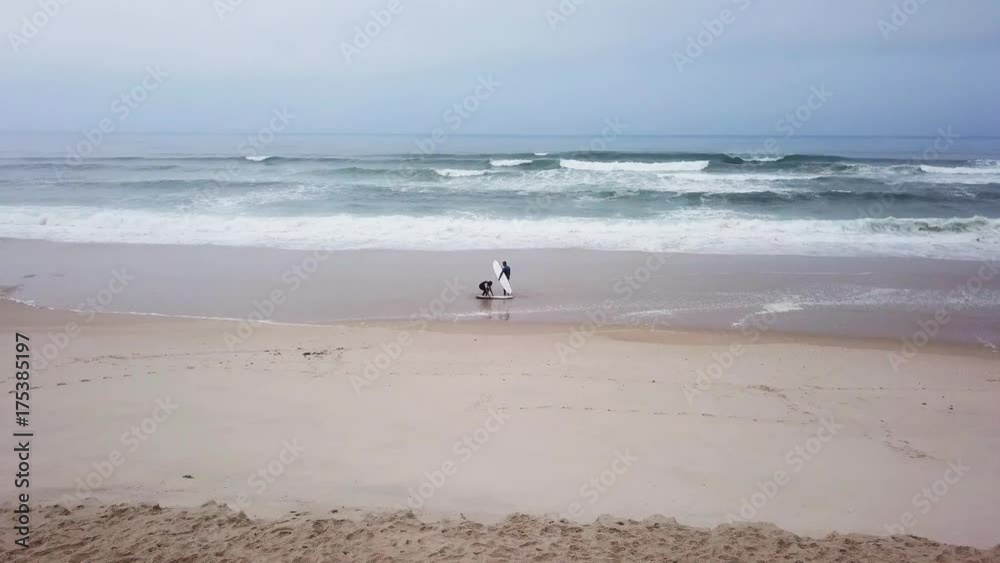 Young couple of friendly surfers wearing wetsuit holding surfboards, walking by the sea on a morning surfing session. Young couple of friendly surfers wearing wetsuit holding surfboards, walking by the sea on a morning surfing session.