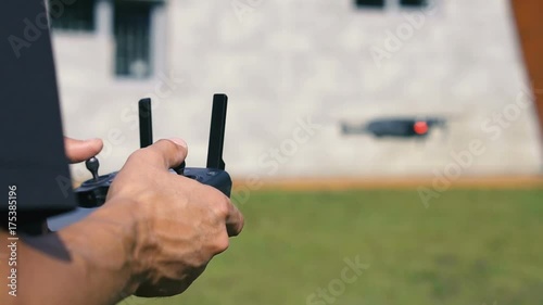 A man controls a drone near a gray building on a green lawn. Summer. Close-up photo