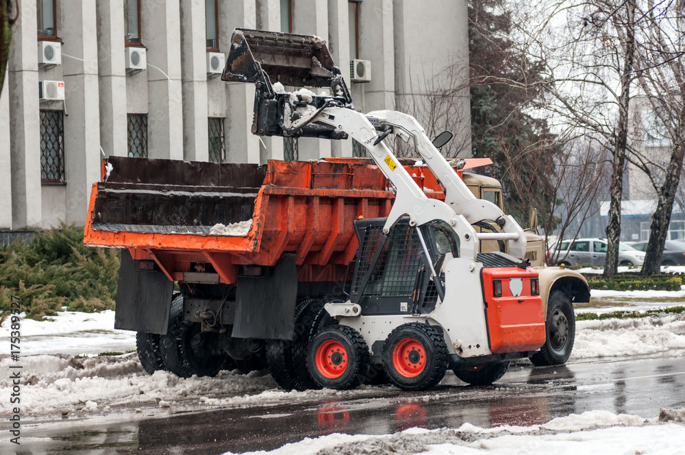 loading snow into a truck on a city street in winter loading snow into a truck on a city street in winter