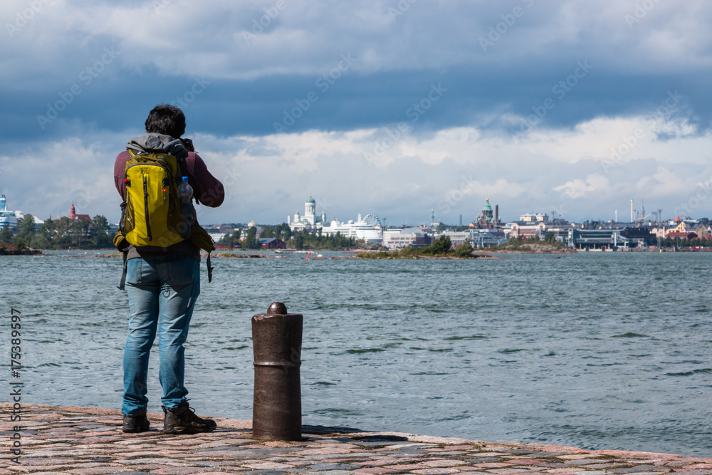 The man photographer stands on the edge of the pier in the fortress of Suomenlinna and takes pictures of the port of Helsinki Finland.