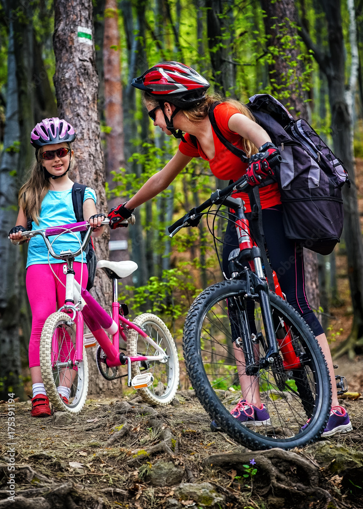 Fototapeta premium Bikes cycling family. Happy mother and daughter wearing helmet are cycling on bicycles into forest. Parenting. Children travel unaccompanied.