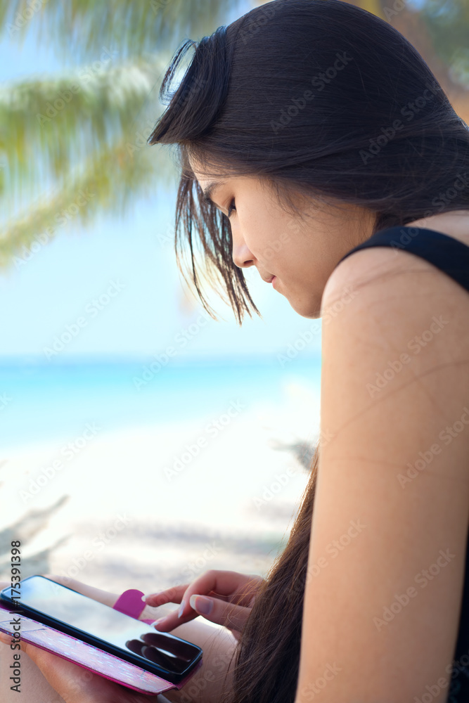 Teen girl on Hawaiian beach using cellphone under coconut trees