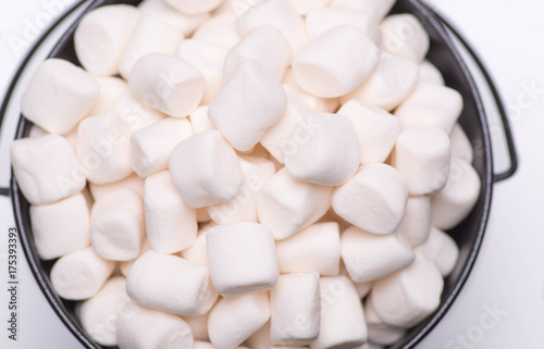 White mini puffy marshmallows ia a black bowl on white background with copy spase. Top view, close-up.