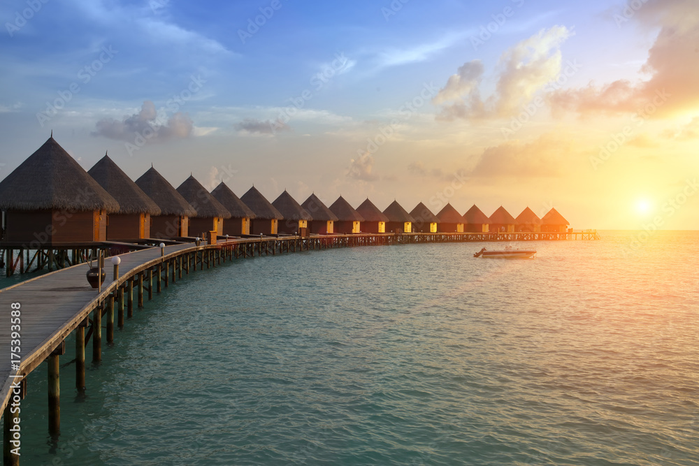 Fototapeta premium houses over the transparent quiet sea water on a sunset. Maldives..