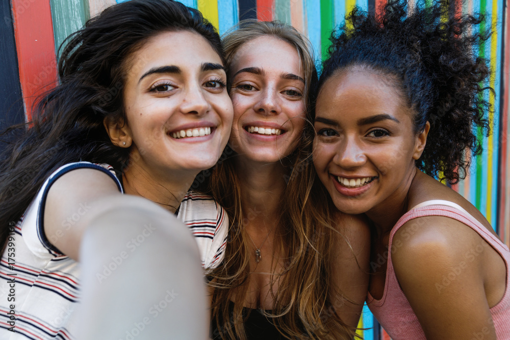 Fototapeta premium Happy friends taking a selfie. Three smiling women looking at camera on a mobile phone.