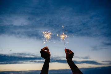 Hands hold sparklers against the night sky