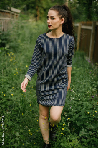 Woman with moody dark makeup walking in tall plants in navy pinstripe dress photo