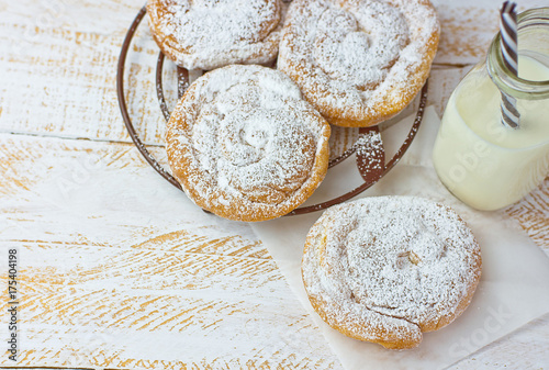 Swirl Danish Pastry Ensaimada Powdered on Cooling Rack and Parchment Paper. Bottle of Milk with Striped Straw. White Plank Wood Tabletop. Top View photo