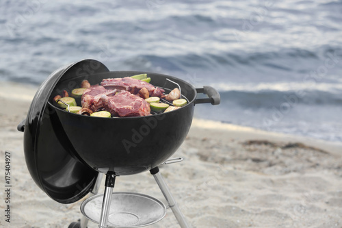 Barbecue grill with tasty steaks and vegetables on beach