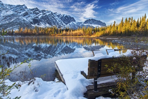 Park Bench on Many Springs lake in Bow Provincial Park at foothills of Rocky Mountains, Alberta, Canada  after early October snowfall with Distant Snowy Mountain Tops Landscape View photo