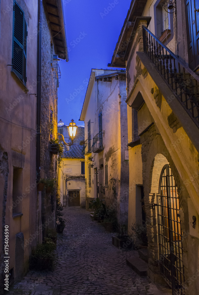 Fototapeta premium Trevignano street at dusk / A typical street of little town of Trevignano Romano, on Bracciano lake, near Rome, Italy at the dusk, nicely illuminated by lamps