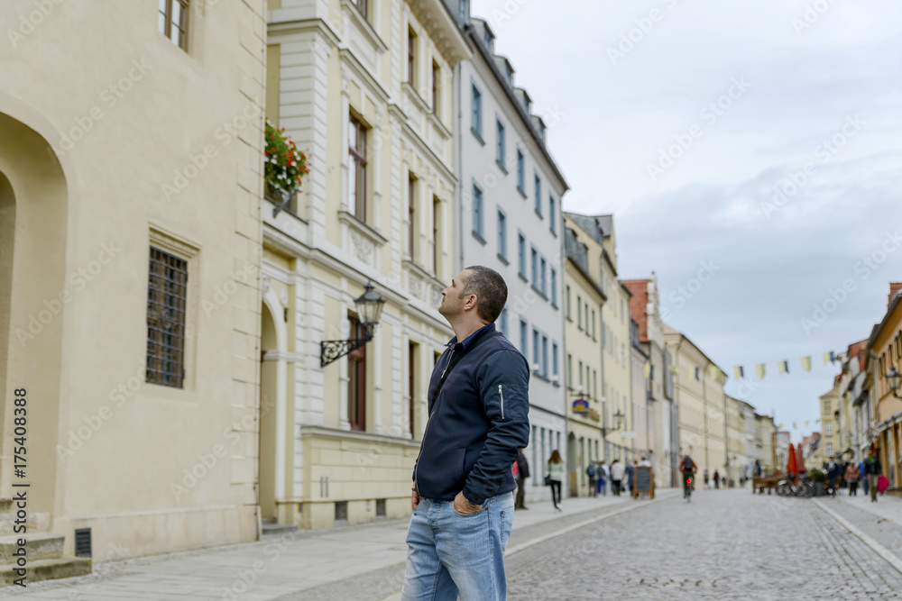 young tourist looks at the sights of a European city, raising his head high young tourist looks at the sights of a European city, raising his head high