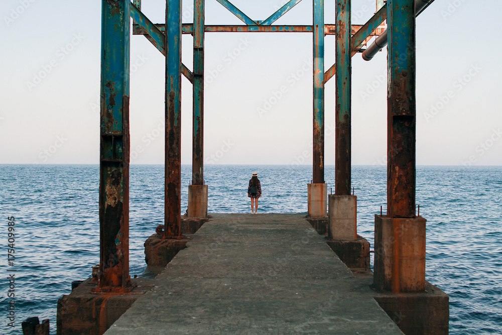 The girl walks on the pier in sunny weather and admires the sea scenery