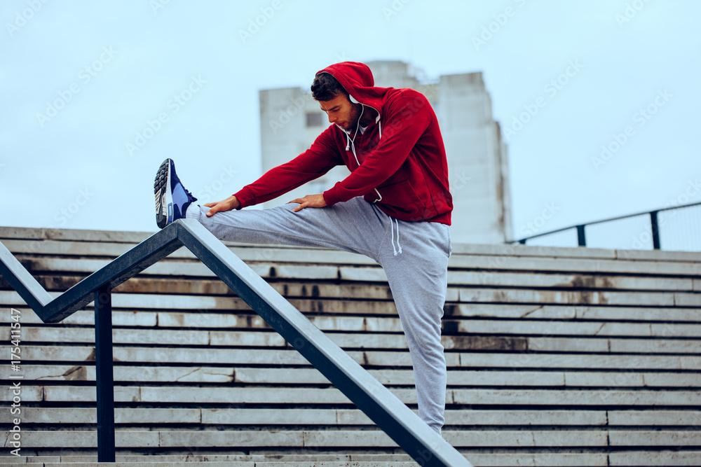 Young fitness man runner stretching legs before running on the stairs