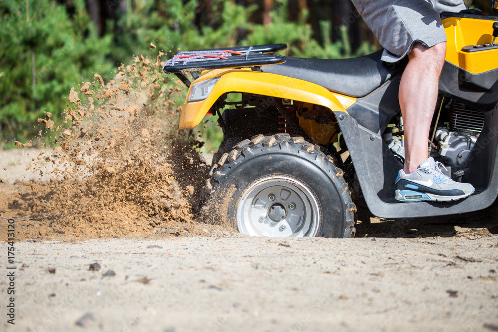 An ATV quadbike get stuck in a sandy road near forest and having wheel-spin making a spray of sand An ATV quadbike get stuck in a sandy road near forest and having wheel-spin making a spray of sand