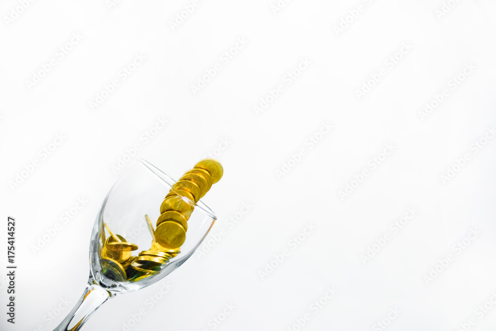 Fototapeta premium Golden coins splash in a glass of champagne on the wall background with copy space.