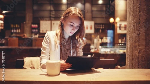 Portrait of Young Woman Using Digital Tablet in Cafe at Night. 4K. Elegant businesswoman drinking coffee, reading news on tablet computer, using app, shopping, communicating in social media. 