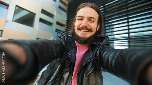 Bearded man taking selfie photos by smartphone before modern building