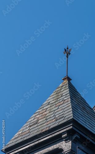 Finial on top of peaked roof. A blue sky is in the background.