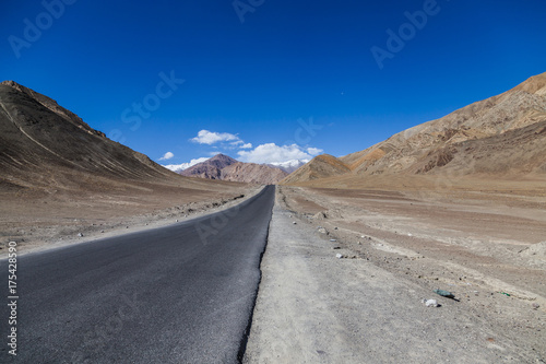 A concrete road towards beautiful rocky mountains and blue sky with peaks of Himalaya, Leh, Ladakh, Jammu and Kashmir, India