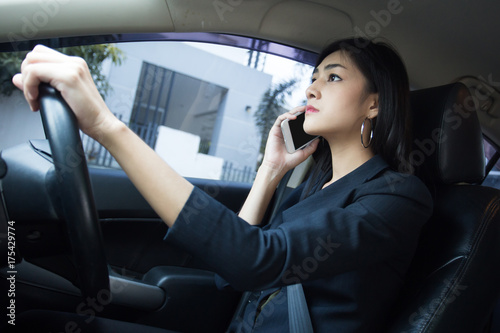 Asian Woman Looking Smartphone while Driving Car to go to Work, Woman working Concept. © Bavorndej