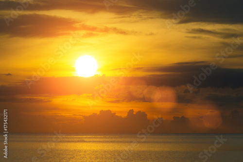 The sun shines through the clouds at dawn on the shore of the Gulf of Thailand. © suwatsilp