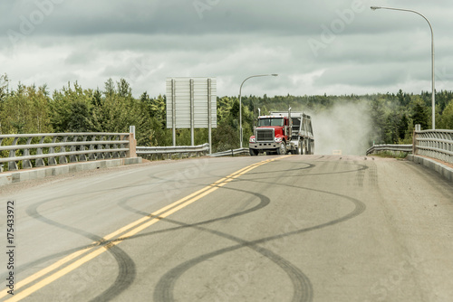 Giant red dump truck makes way down to the trans canada on road with tire markings