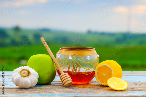 Fresh honey in glass jar, honey dipper , green apple, garlic and lemon on old wooden with blurred background , healthy nutrition and strengthening immunity . photo