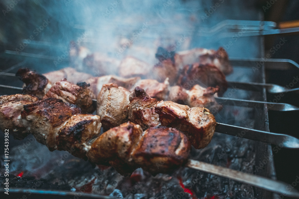 Grilled kebab cooking on metal skewers (grill). Roasted meat cooked at barbecue with smoke. Close up BBQ fresh pork meat chop slices. Traditional eastern dish, shish kebab. Grilled kebab cooking on metal skewers (grill). Roasted meat cooked at barbecue with smoke. Close up BBQ fresh pork meat chop slices. Traditional eastern dish, shish kebab.