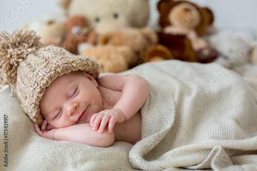 Little newborn baby boy, sleeping with teddy bear at home in bed