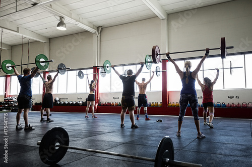 Rear View Of Clients Lifting Barbells In Gym