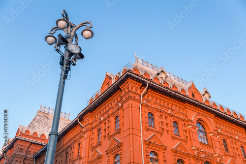 Light post and old orange building called State Historical Museum of Red Square in Moscow, Russia with sunlight and blue sky background.