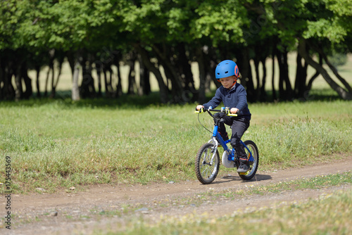 Happy kid boy of 5 years having fun in spring forest with a bicycle on beautiful fall day. Active child wearing bike helmet.