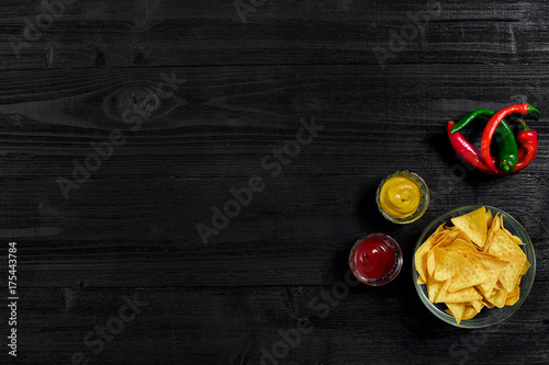 Glass plate with corn chips nachos and tomato sauce on a black wooden table top view. Place for text