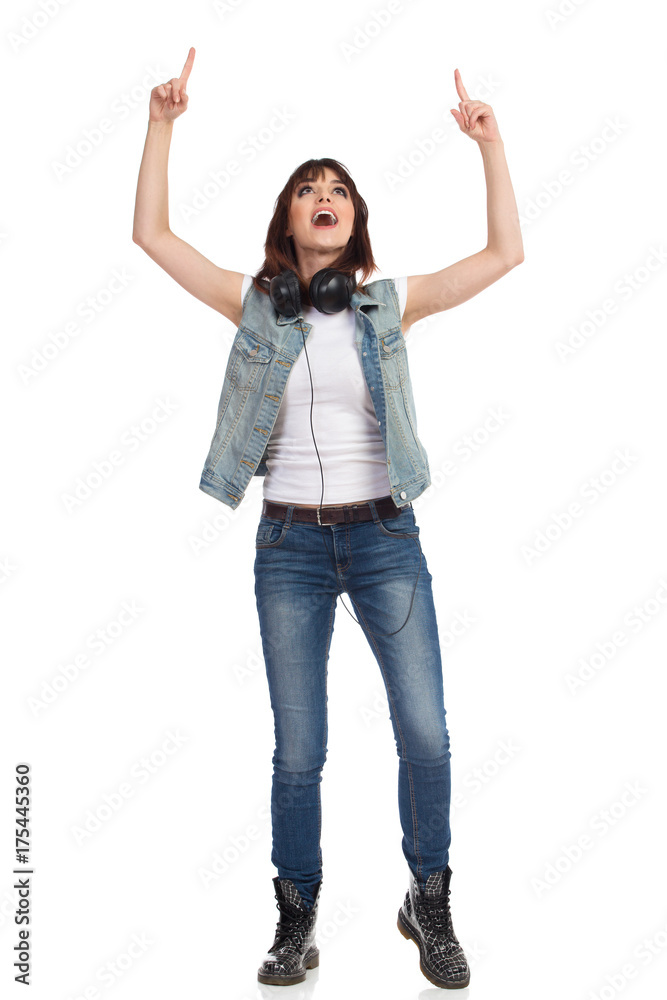 Young Woman In Jeans Unbuttoned Vest Is Standing, Pointing Up And Talking Young Woman In Jeans Unbuttoned Vest Is Standing, Pointing Up And Talking