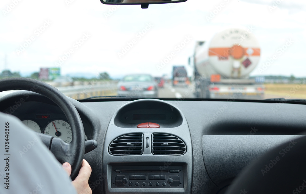 Man driving a car on a highway in a traffic jam with a tank and other vehicles blurred in front of him