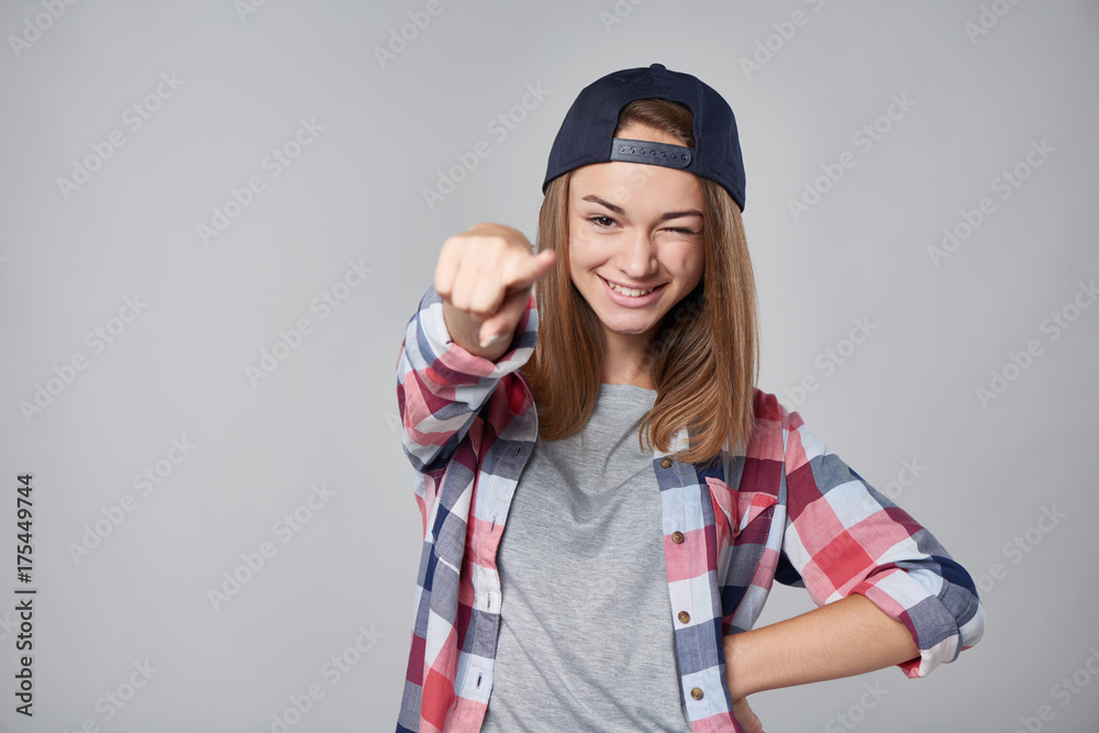 Emotional teen girl winking and pointing at camera over grey background. Half length portrait with copy space Emotional teen girl winking and pointing at camera over grey background. Half length portrait with copy space