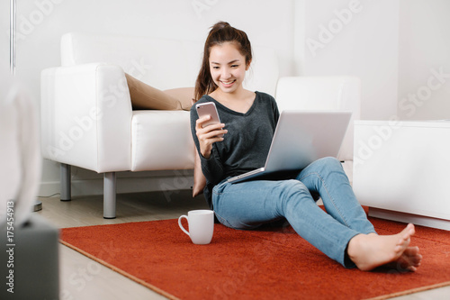 Attractive young Asia woman reading message on her cellphone in living room